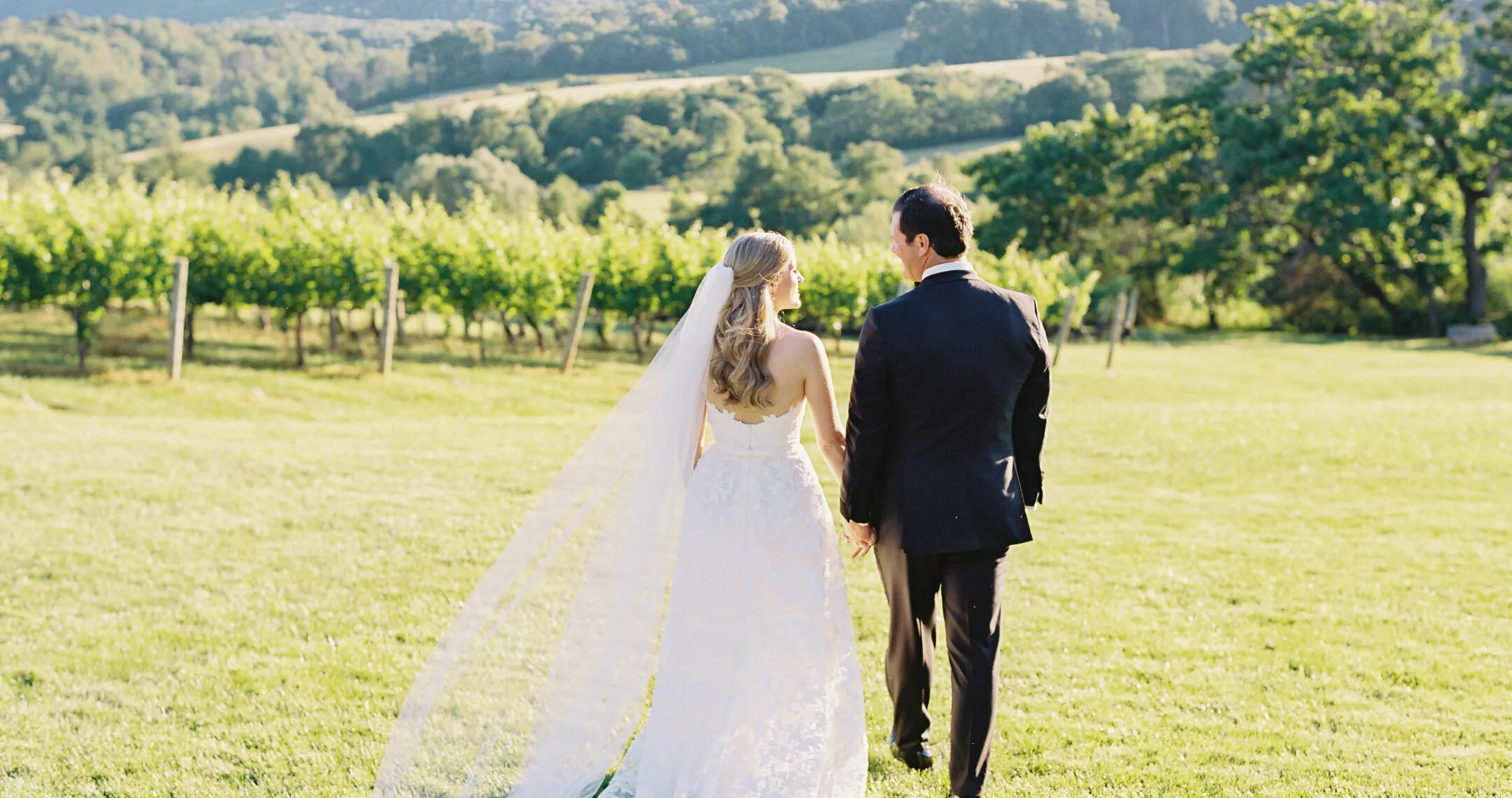 A bride and groom walking in a green hilly landscape