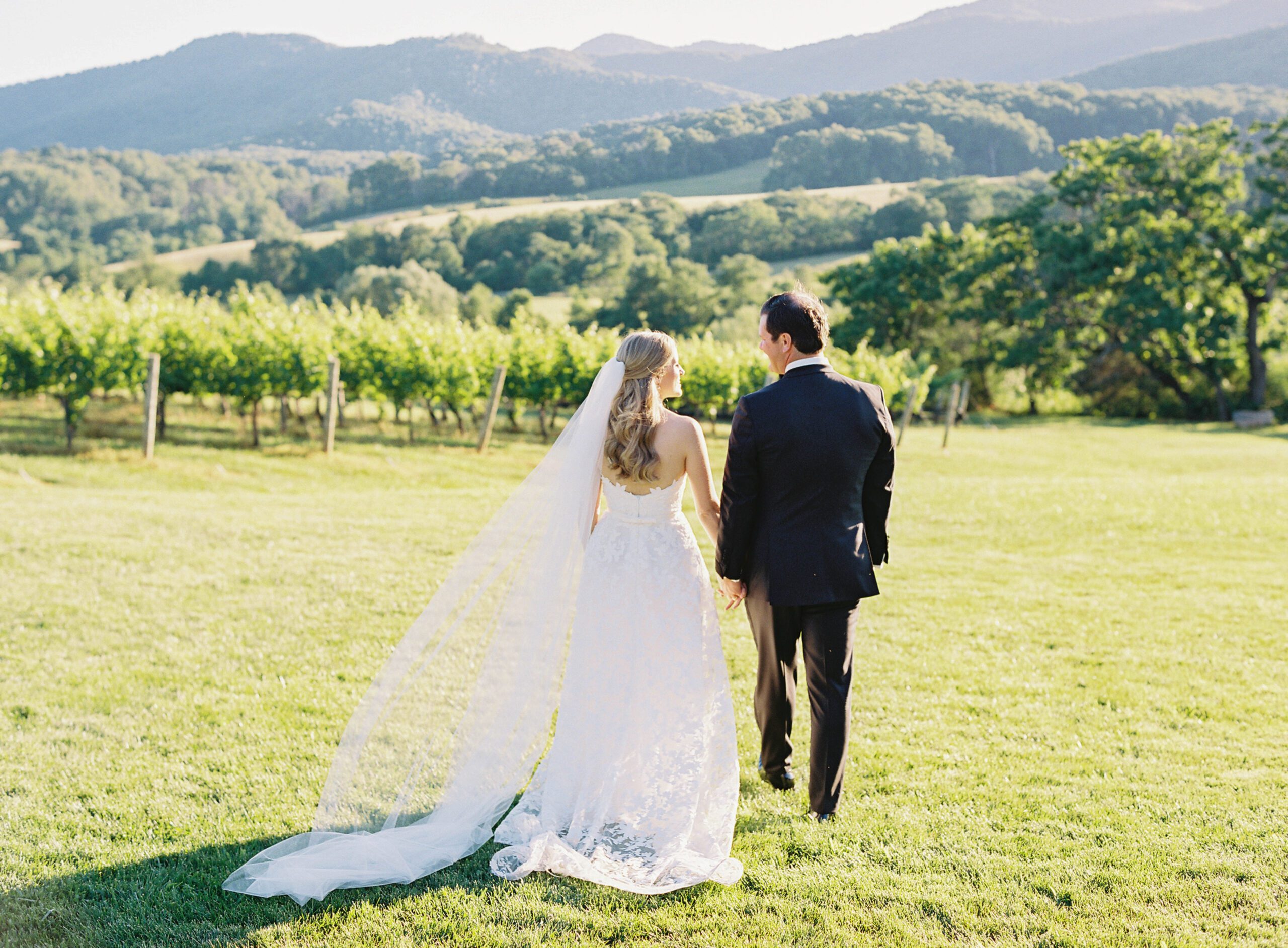 A bride and groom walking in a green hilly landscape